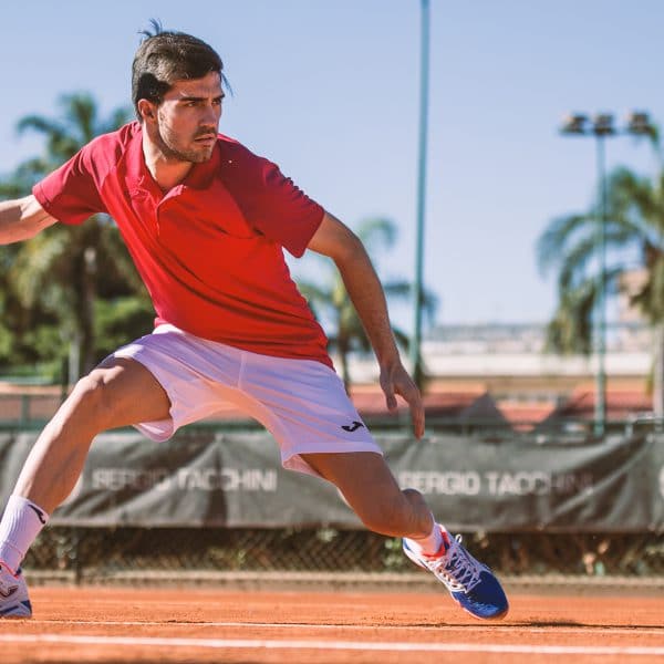 Tennis player hotting a ball in red and white Joma kit