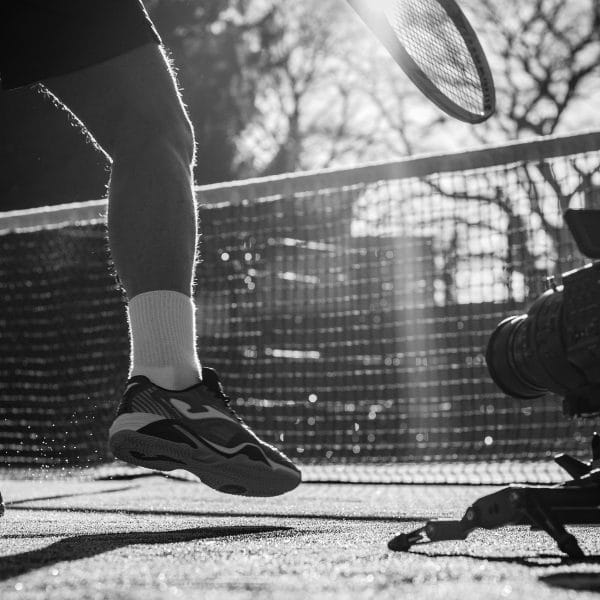 A photograph of a video camera on a tennis court whilst someone is playing