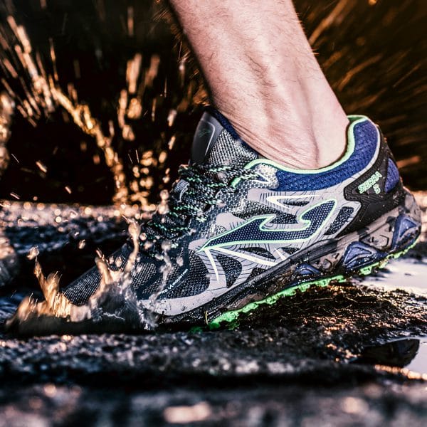 A close up photograph of a Joma trainer splashing in a puddle